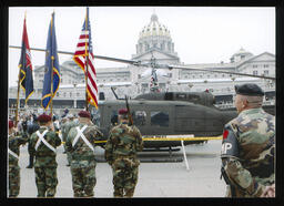A side view of the helicopter known as "America's Huey - 091" resting on Commonwealth Avenue with the State Capitol building in the background.
